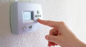 Finger pressing the down button on a wall-mounted thermostat.