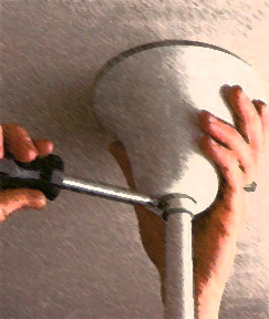 Hands using a screwdriver to install a ceiling fan canopy. 