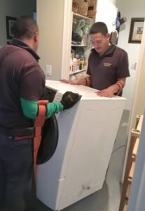Man’s hand installing two labeled hoses at the back of a washer.