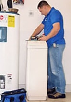 Man installing a water softener beside a water heater.