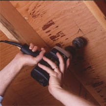 Man's hands drilling underneath the floor using a hole saw.