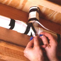 Man's hands connecting central vacuum wires on piping underneath the floor.