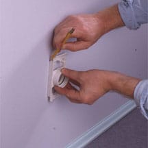 Man's hands marking an inlet valve's position on a wall.