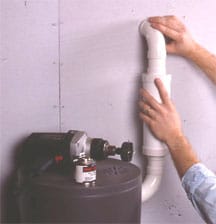 Man's hands connecting a pipe from vacuum power unit through a wall.
