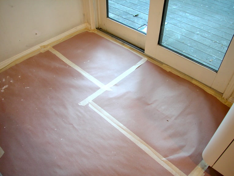A paper drop cloth sealed by masking tapes onto a room's floor.