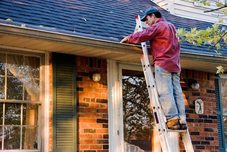 Man working on a house’s rain gutter using a step ladder.