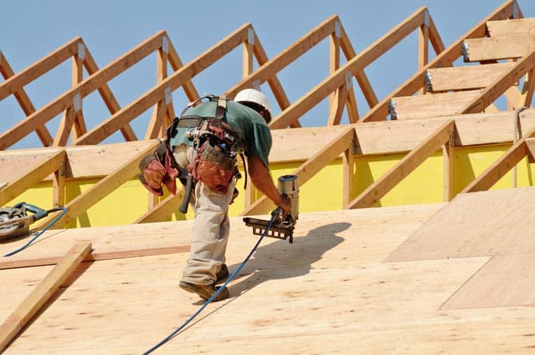Carpenters nail plywood sheathing to the roof rafters—in this case, a series of roof trusses.