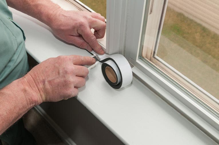 Man's hands cutting an adhesive-backed foam window weather stripping.
