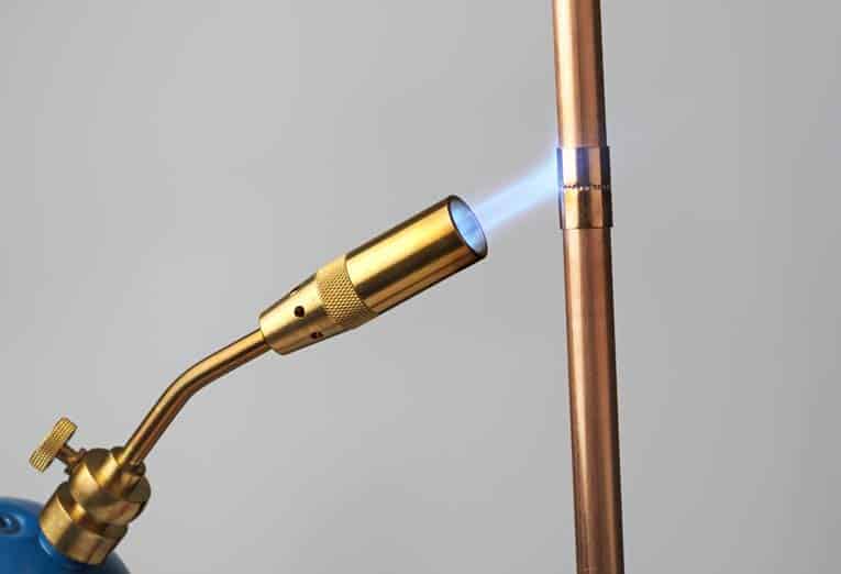 Heat the fitting with a propane torch. Test it by touching the joint between pipe and fitting with solder wire—when it readily melts, solder the connection.