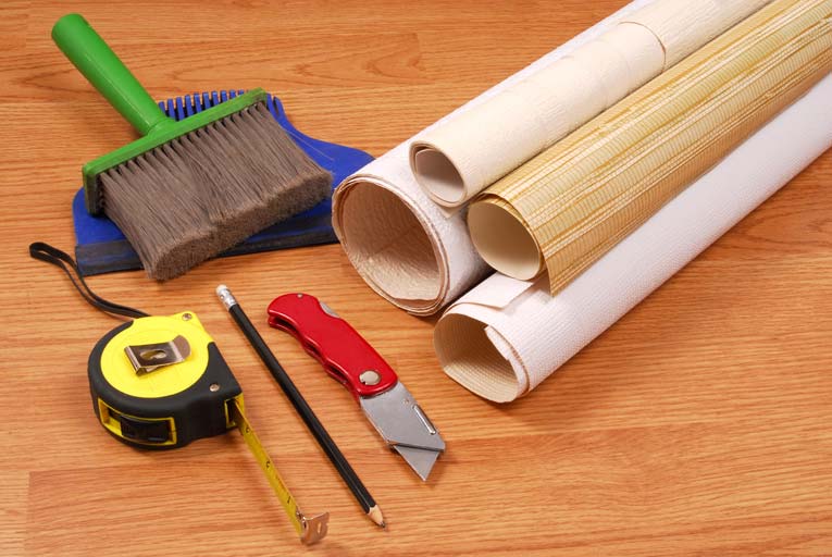 wallpapering tools on table, including brush, tape measure, pencil, and utility knife