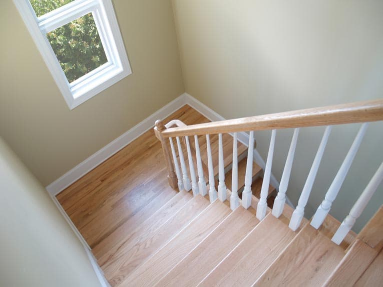 Bird's eye view of a wooden stairway with white rails.