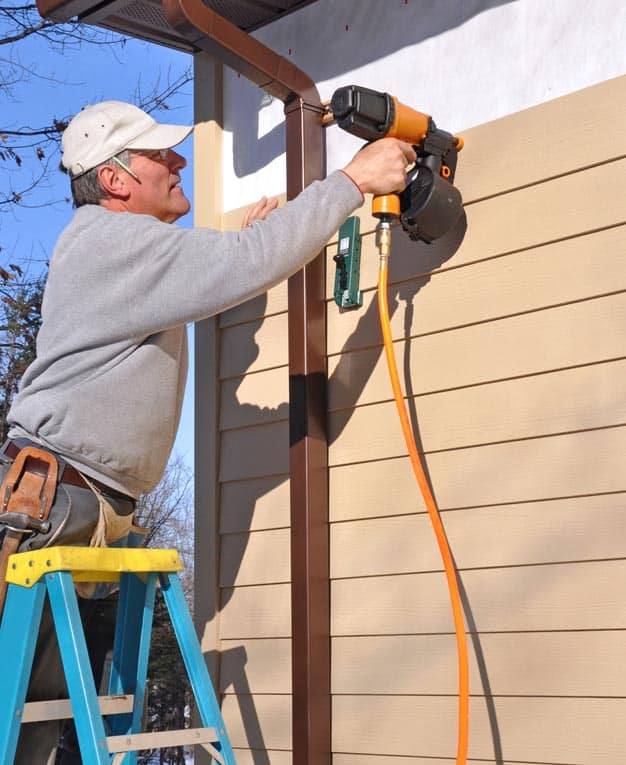 Man installing a fiber-cement wall siding with a nail gun.