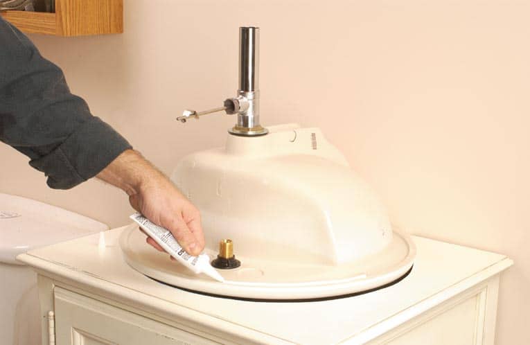 Man applying sealant around the rim of the sink as it lays upside-down.
