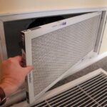 Man’s hand removing an air conditioner filter on a wall return-air register.