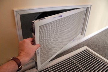 Man’s hand removing an air conditioner filter on a wall return-air register.
