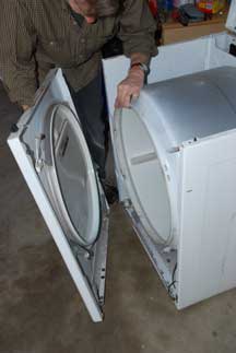 Man supporting a clothes dryer’s tumble drum, while removing a front panel.