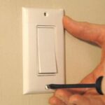 Man's hand unscrewing a white light switch face plate.