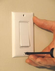 Man's hand unscrewing a white light switch face plate.