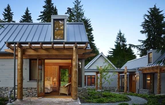 Three farmhouses in sheet-like metal panel roofing with 2 flat roof dormers, a rustic exterior design, and an outdoor landscape.