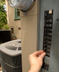 Hand switching off an outdoor circuit breaker with a central AC compressor in the background.