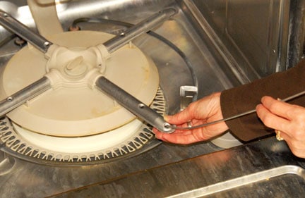 Man’s hands cleaning a dishwasher’s bottom spray hole with a stiff wire.