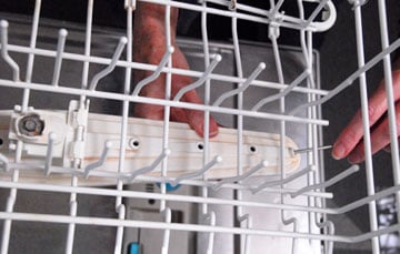 Man’s hands cleaning a dishwasher’s top spray hole with a stiff wire.