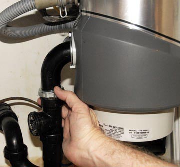 Man's hand connecting a garbage disposal's tailpiece to a drain pipe.