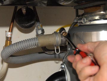 Man's hand tightening a dishwasher's drain hose clamp using a screwdriver.