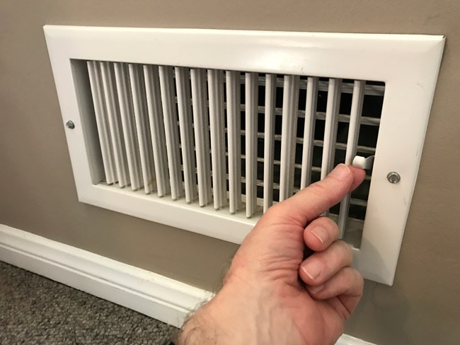 A hand using the lever on a heating register to open the vent. 