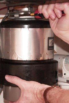 Man's hands turning a garbage disposal's top using a screwdriver.