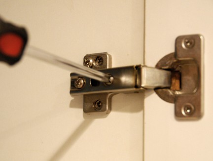 Adjusting a European-style hinge using a screwdriver.