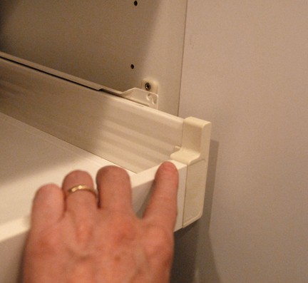 Man’s hand holding a white sliding shelve with a missing mounting screw.