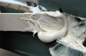 A flat stick filling a rotten wood part with epoxy putty.