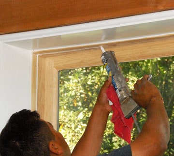 A man applying caulk on a window molding.