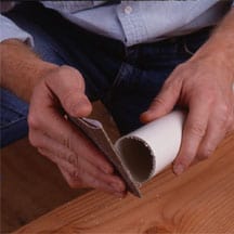 Man's hands sanding a rough PVC pipe edge.