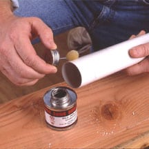 Man's hands applying PVC cement around a pipe's end.