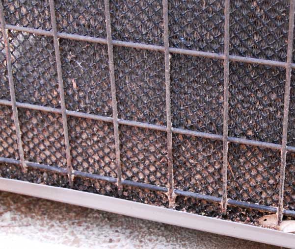 The outer portion of a central air conditioner's coils, caked with dirt. 