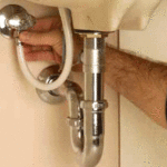 Man’s hand turning a water supply valve underneath a sink.