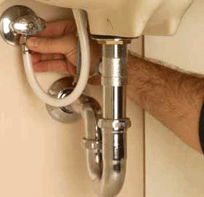 Man’s hand turning a water supply valve underneath a sink.