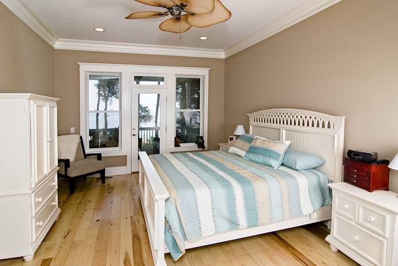 A beach house bedroom with wood floors, crown molding, and tropical ceiling fan. 