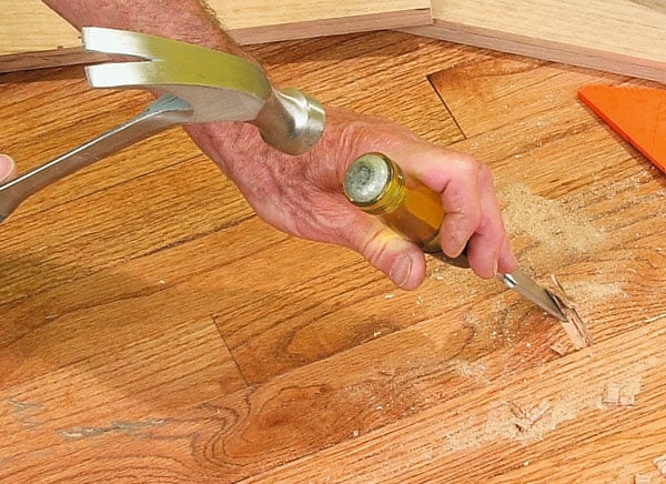 Man's hands hammering a chisel, cutting out part of a wooden floor.