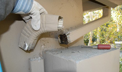 Man's hand holding a detached elbow pipe clogged with debris.