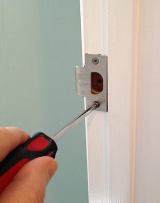 Man's hand screwing a door jamb's strike plate.