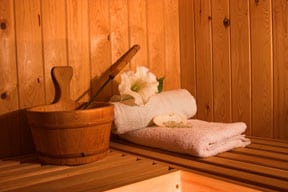 A wooden bucket, ladle, and towels on a sauna's bench.