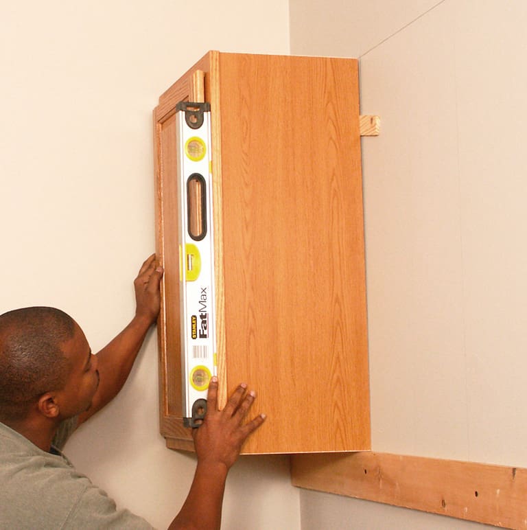 Support upper cabinets on a temporary rail. Then level and shim them before fastening them to wall studs.