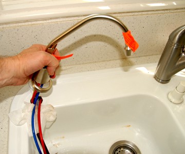 Man's hand installing a water dispenser with tubings in a sink hole.