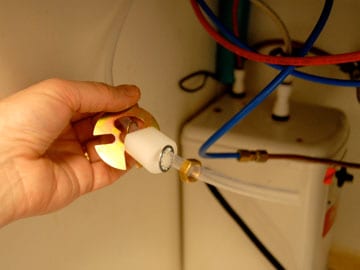 Man's hand holding a transparent plastic tubing from a water dispensing tank.