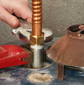 Man's hand loosening a nut on a water line using a wrench.