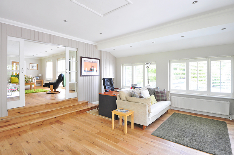 A bright room featuring a white couch, light wood flooring, and lots of windows.