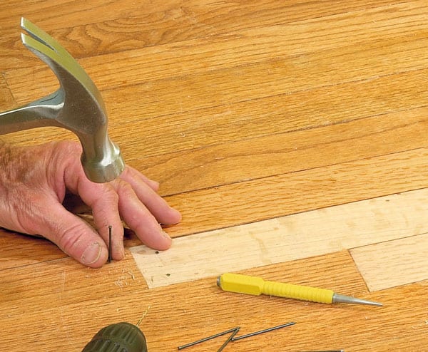 Man's hands nailing a replacement wooden floor board.